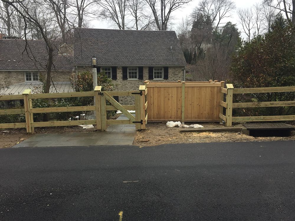 A wooden fence and gate in front of a stone house on a gray day.