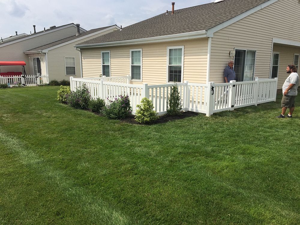 Backyard view of a house with white picket fence, green lawn, and two men standing nearby.