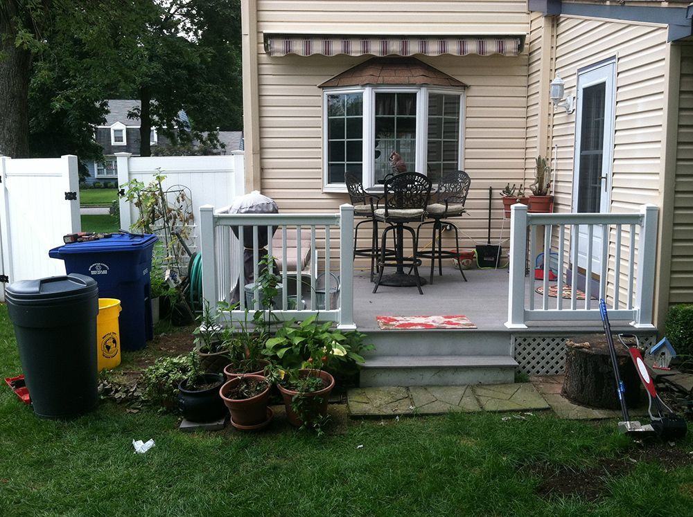 Backyard with deck, outdoor furniture, plants, trash cans, and a house with an awning.