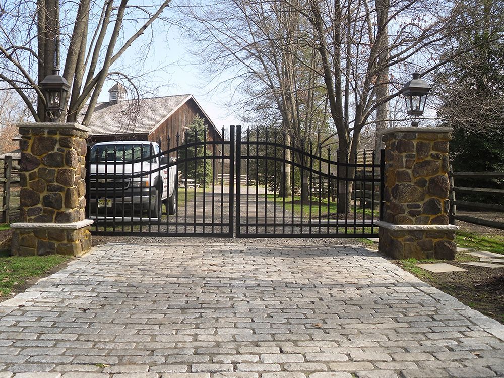Black metal gate between stone pillars, leading to driveway and barn.