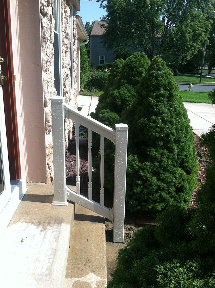 White railing on a concrete step next to a stone house with greenery.