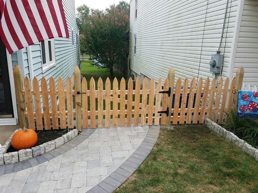 Wooden picket fence with a gate between two houses, fronted by a stone path and grass. A pumpkin sits to the left.