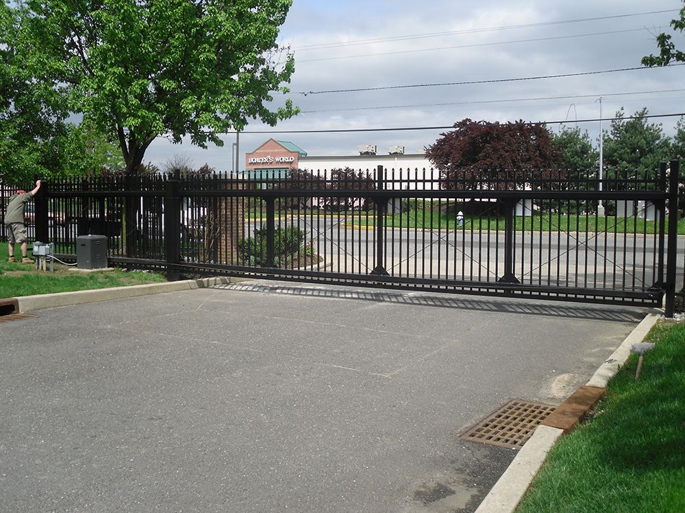 Black metal security gate across a paved driveway, a building in the background.