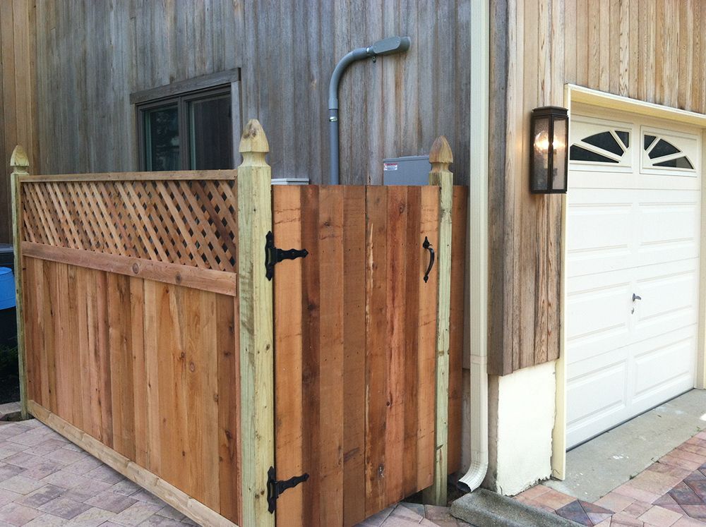 Wooden fence with gate next to a garage, including a light fixture, downspout and outdoor shower head.