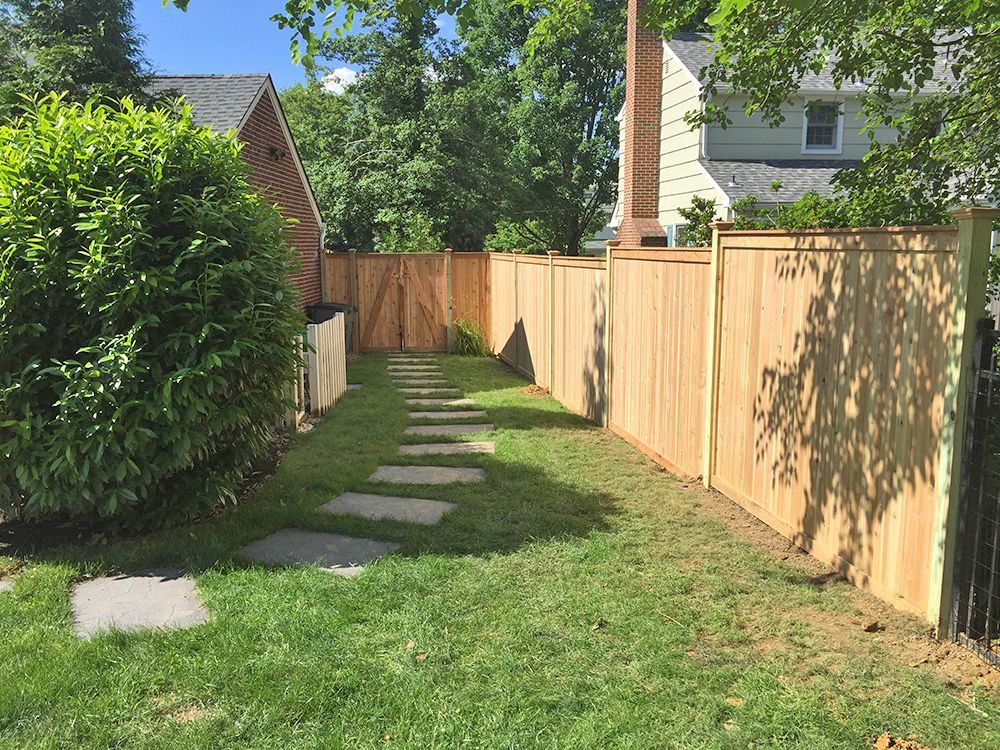 A backyard with a wooden fence, stone path, and green grass.