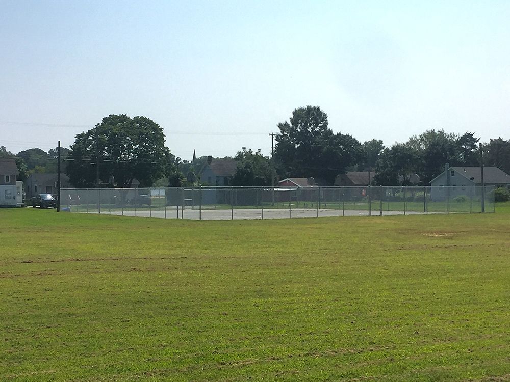 A circular fenced-in area on a grassy field with trees and houses in the background under a clear sky.