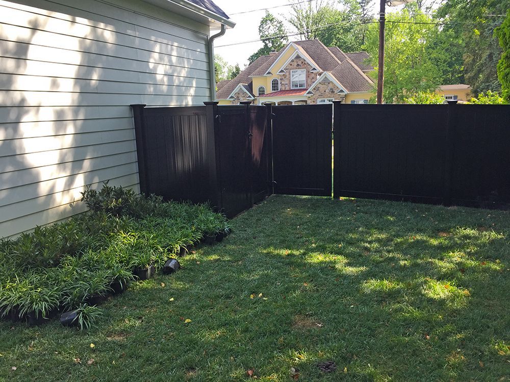 Black fence surrounding a green lawn next to a light-colored house.