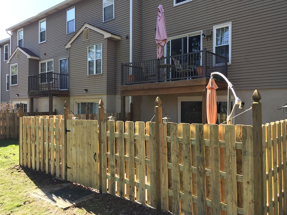 A wooden picket fence surrounds a backyard patio. A two-story building is in the background.