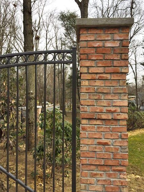 Brick pillar with a black metal gate in front; trees in the background.