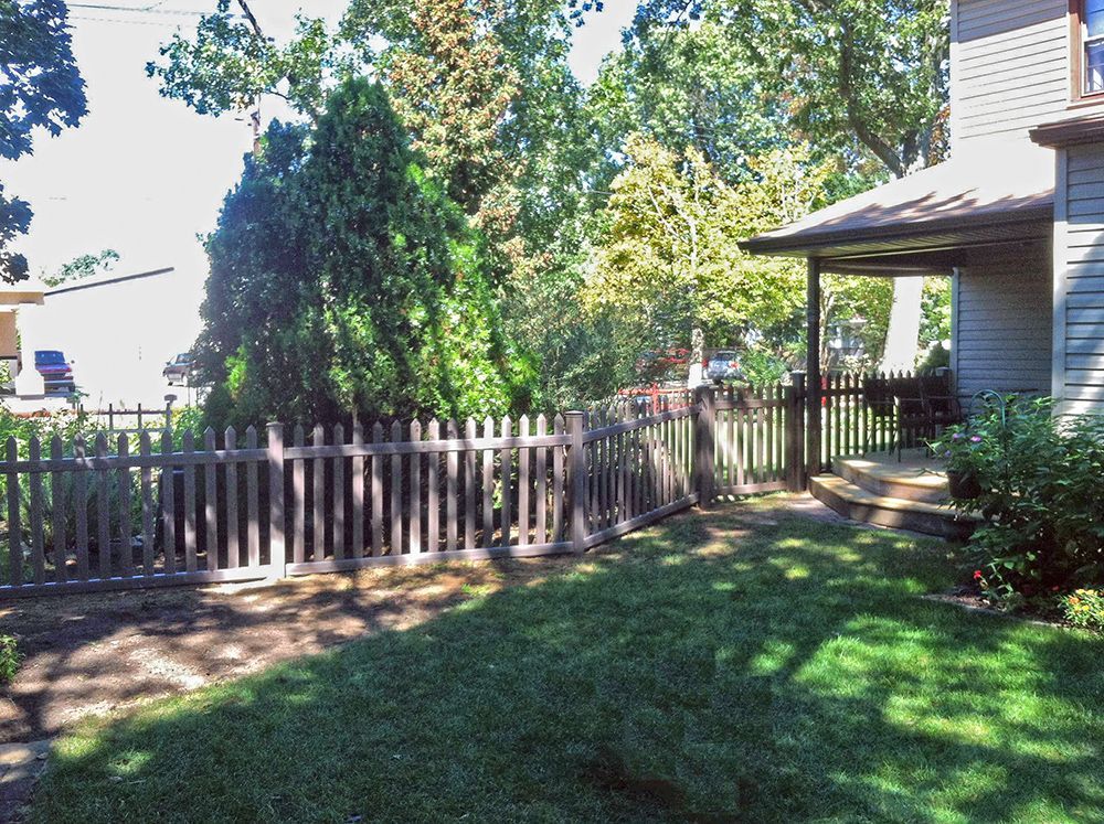 Lawn with wooden fence and gate, leading to a porch next to a house, surrounded by trees.