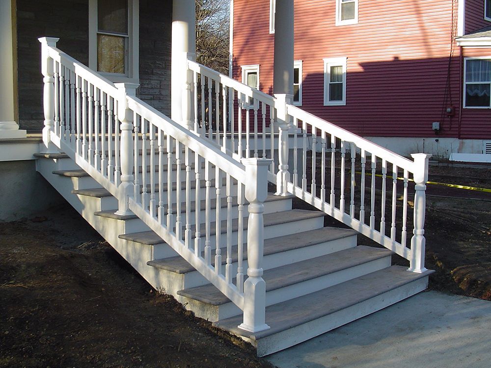 White staircase with railing leads up to a house porch; steps are light brown; red building in background.