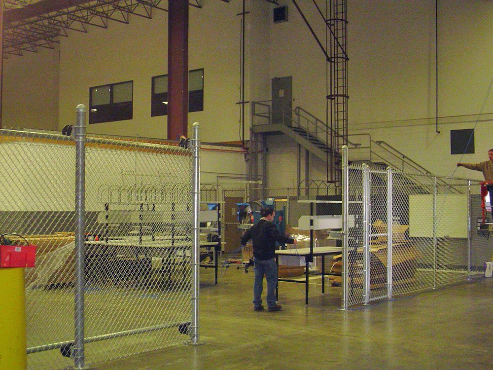 Warehouse interior with chain link fences and two people near machinery.
