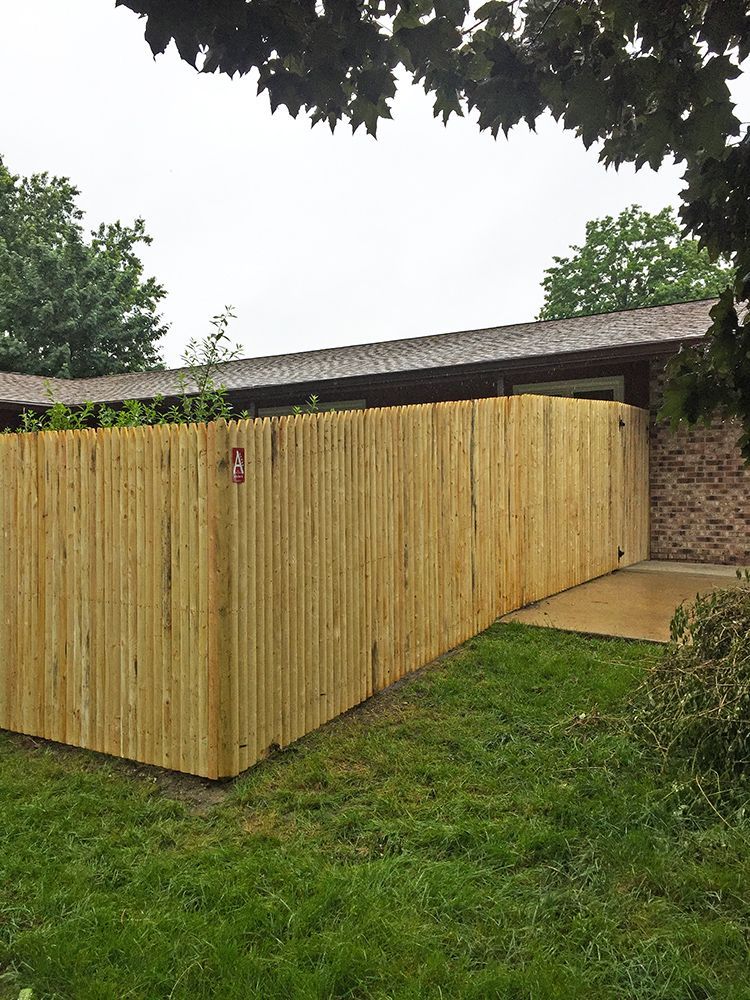 Wooden privacy fence next to a brick building and green grass on a cloudy day.