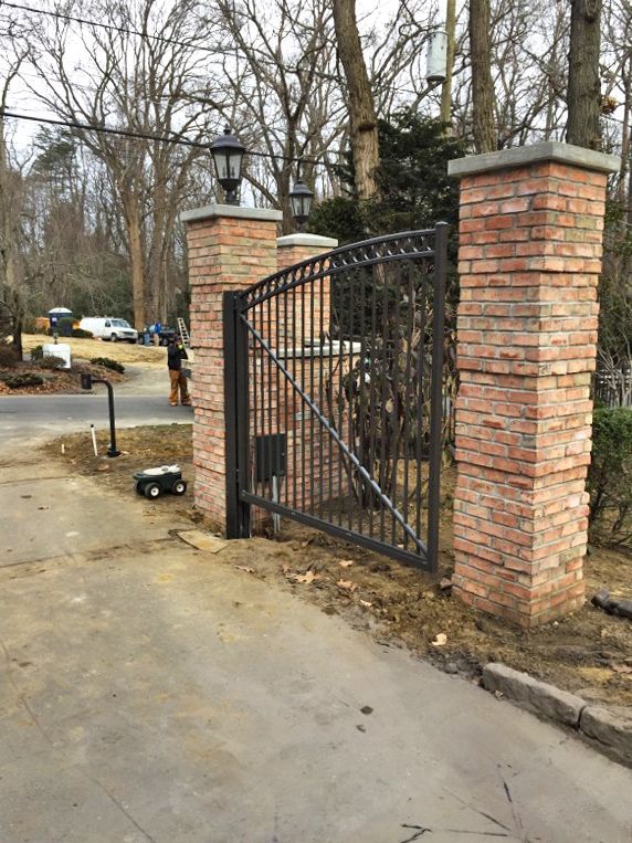 Brick columns with a black metal gate and lampposts. Gray driveway.