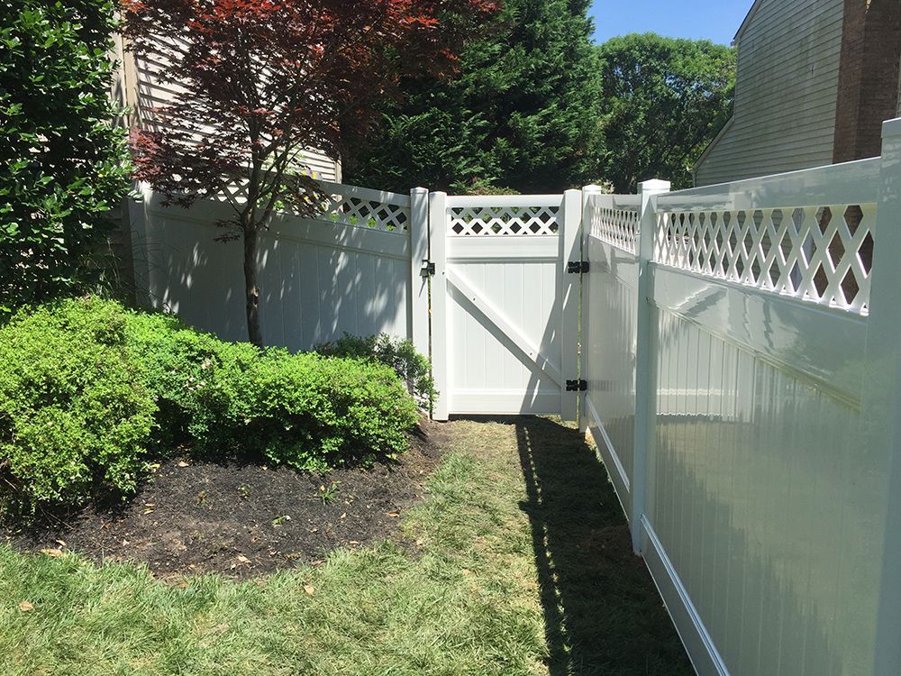 White vinyl fence with gate in a yard with green grass and a bush.