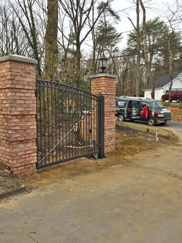 Brick gate posts with iron gate. A black van is parked nearby.
