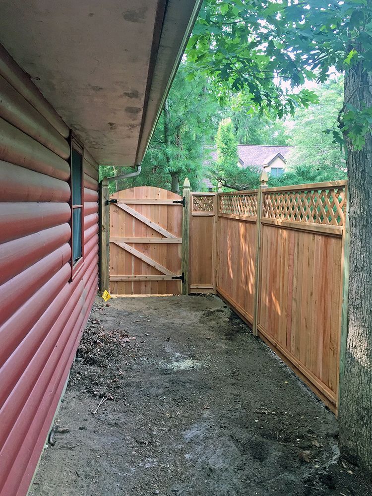 Wooden fence and gate along the side of a red log cabin.