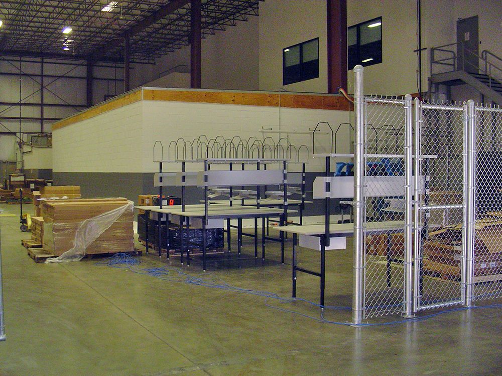 Warehouse interior with workstations and security fencing.