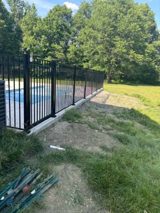 Black metal fence around a pool, on a concrete base, with a grassy lawn and trees in the background.