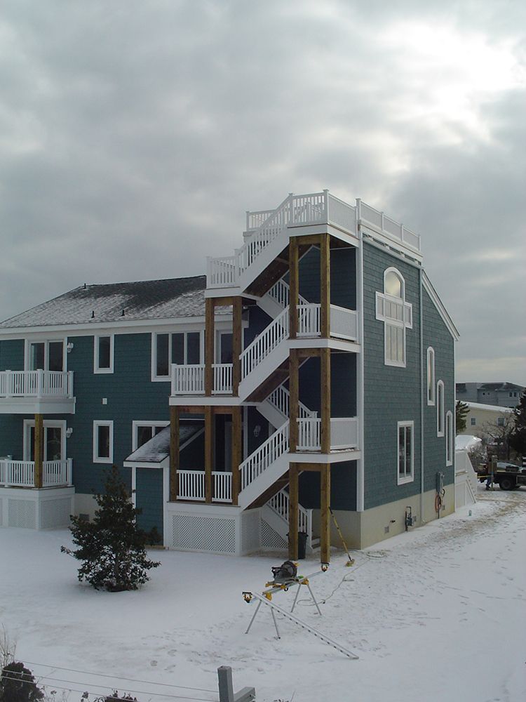Blue house with external staircases on a snowy day. White railing, cloudy sky.