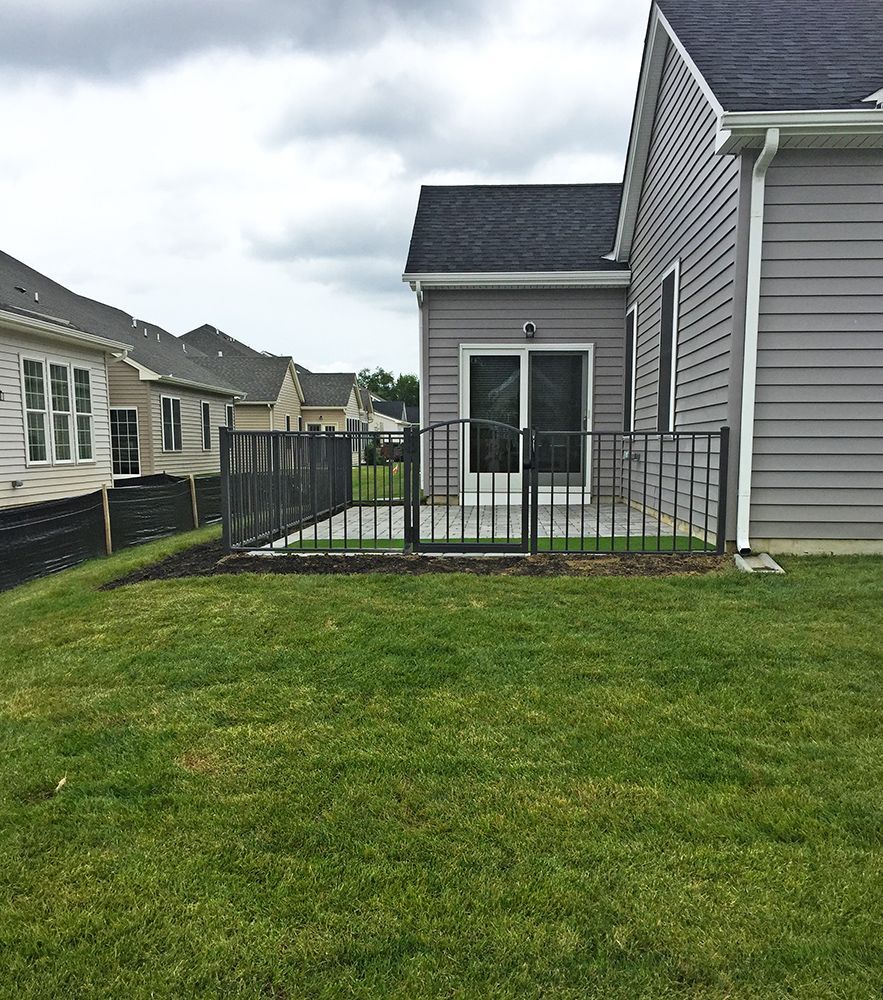 A fenced patio outside a gray house with a sliding glass door, grass in the foreground, and other houses in the distance.