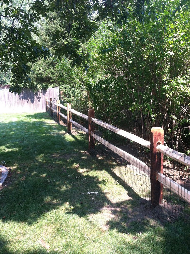 Two-rail wooden fence with dark posts, along a green lawn and trees.