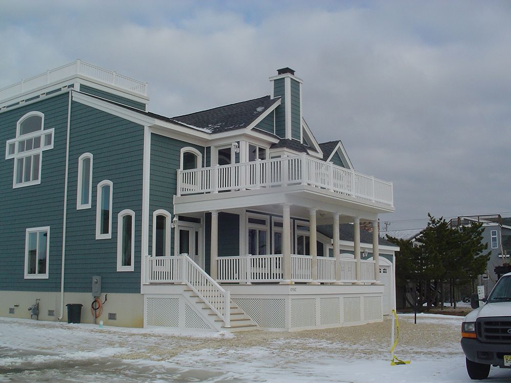 Two-story teal beach house with white trim and balconies, snowy ground.
