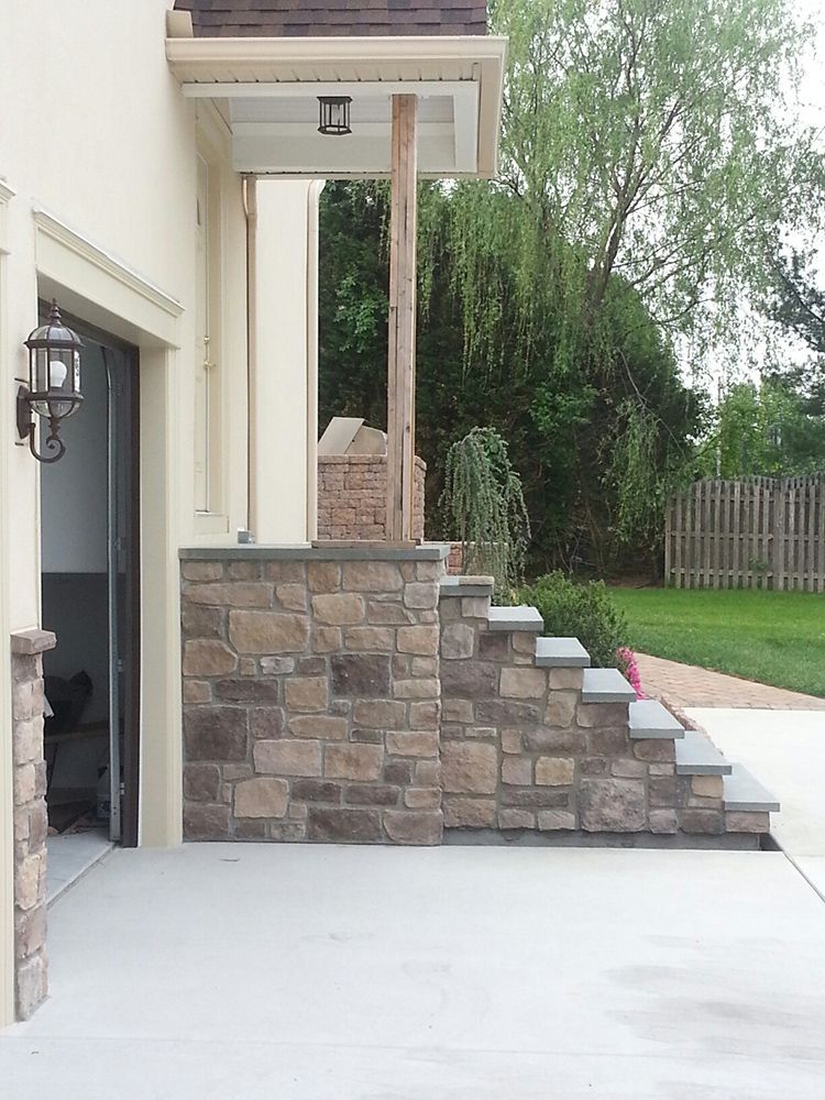 Stone steps lead up to a porch with a wooden post. Garage door and lamppost on the left.