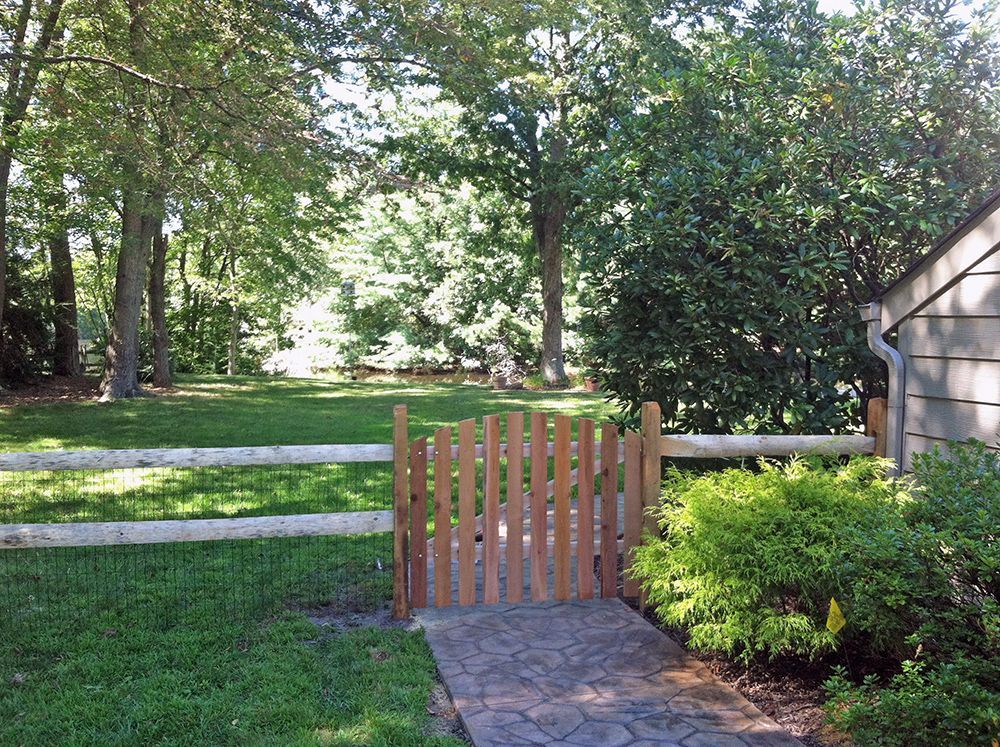 Lush green yard with a wood fence and gate leading to a backyard with trees.