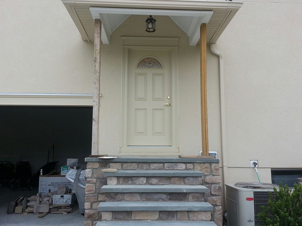 Beige front door with porch, stone steps, and garage on the left.