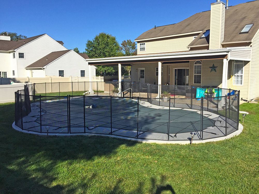 Backyard with a swimming pool surrounded by a black mesh fence. A house with a covered patio is in the background.