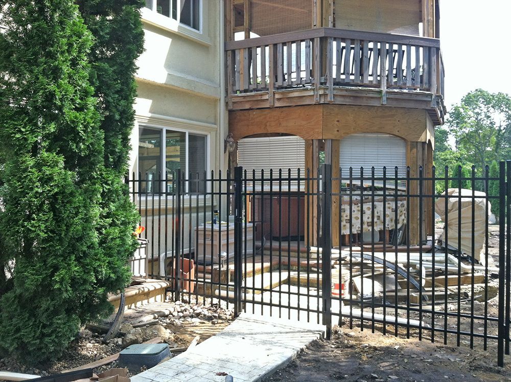 Black metal fence in front of a house. A second-story wooden deck is visible above.