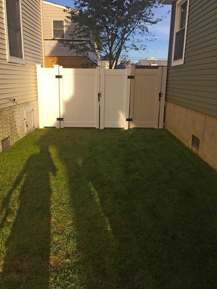 White fenced yard with green grass and shadows. Two houses flank the yard.