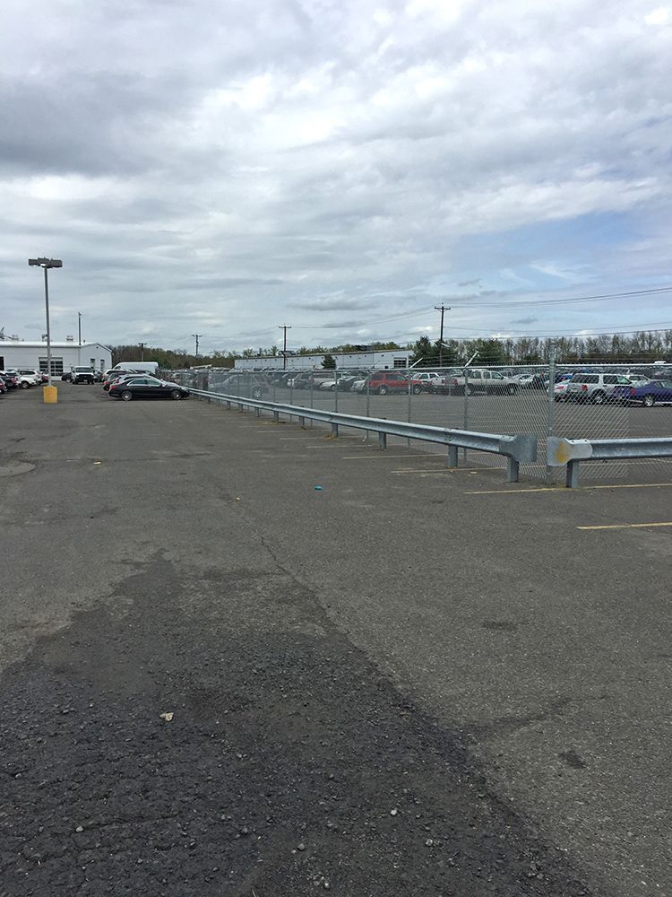 Empty asphalt parking lot with metal barriers, cars, and overcast sky.