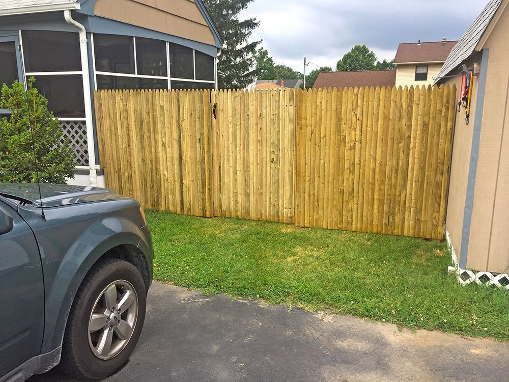 Wooden fence in a yard with green grass, a car, and part of a house.