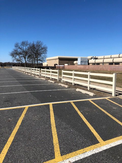 Empty parking lot with yellow lines, white fence, and a building on a sunny day.