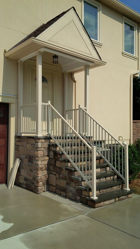 Beige house with porch, stone steps, white railing, and a tan roof.