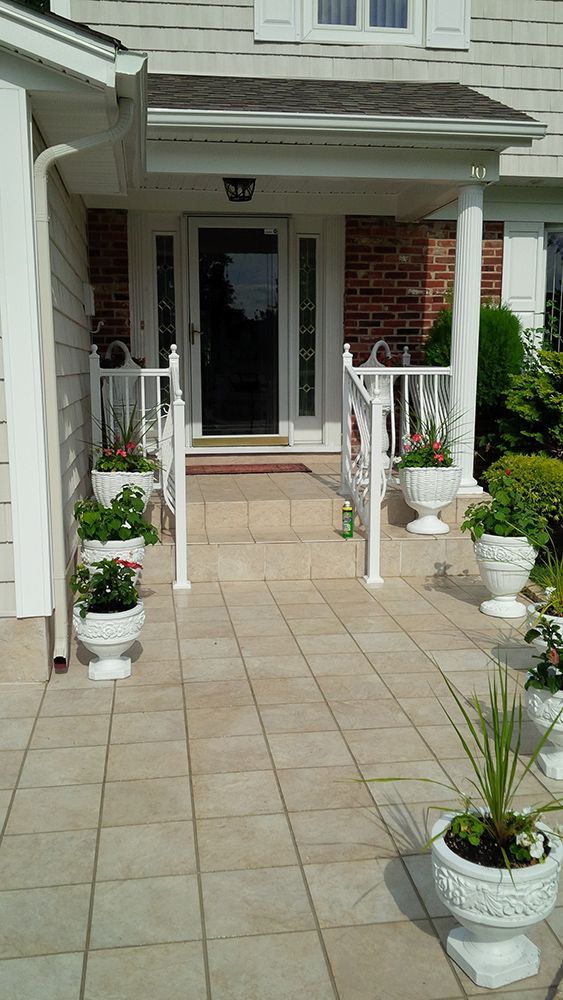 White-columned porch with several white planters filled with colorful flowers.