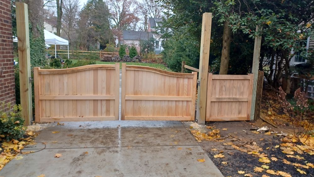 Wooden driveway gates, light brown, set on concrete, with supporting posts; fall leaves in view.
