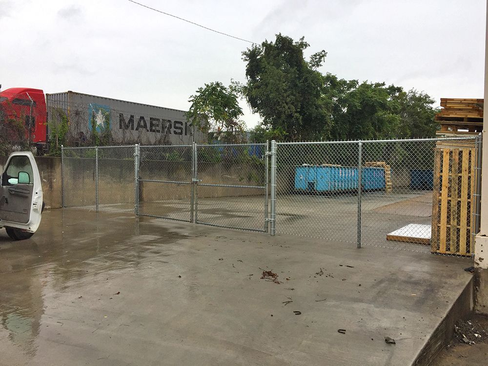 A chain-link fence encloses an industrial area, with a van parked nearby and a Maersk container visible.