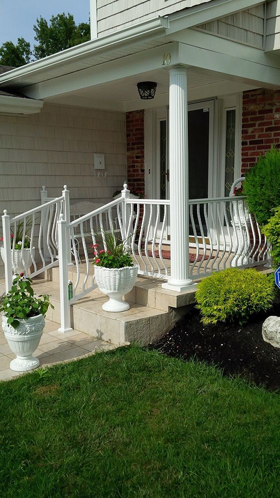 White porch with decorative railing and potted plants in front of a house.