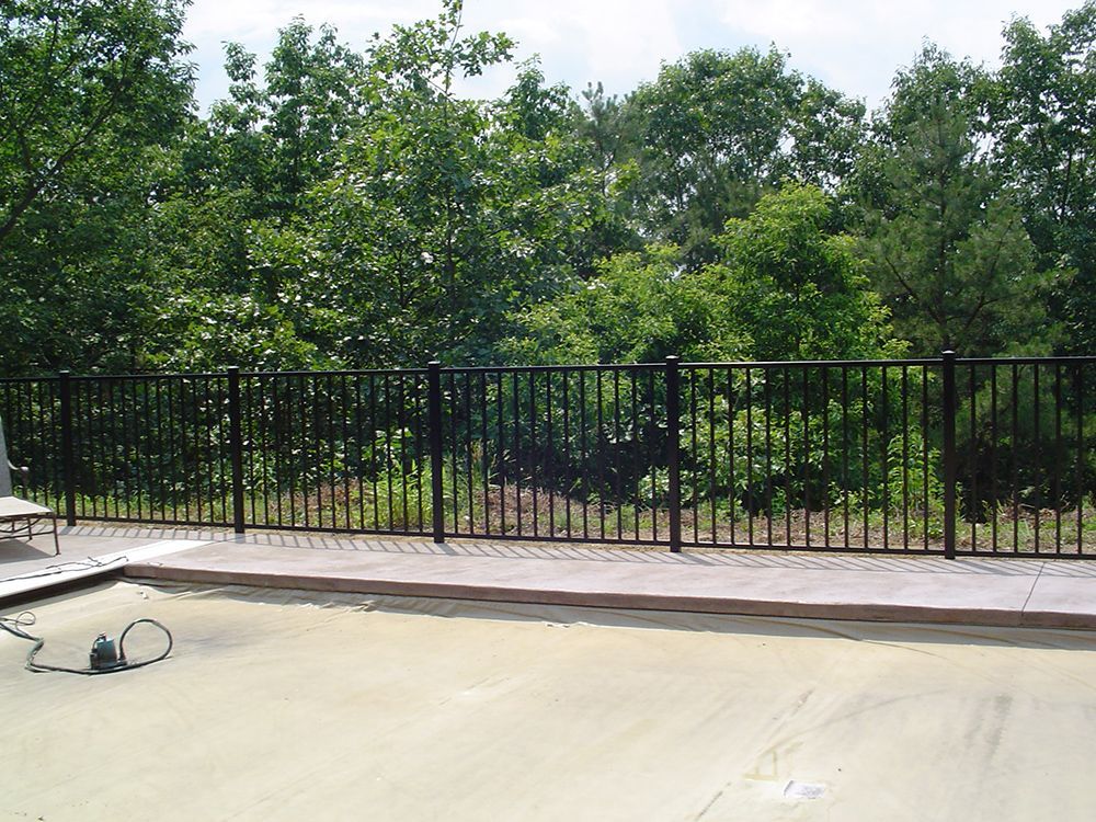 Black metal fence on a concrete surface, with trees in the background.