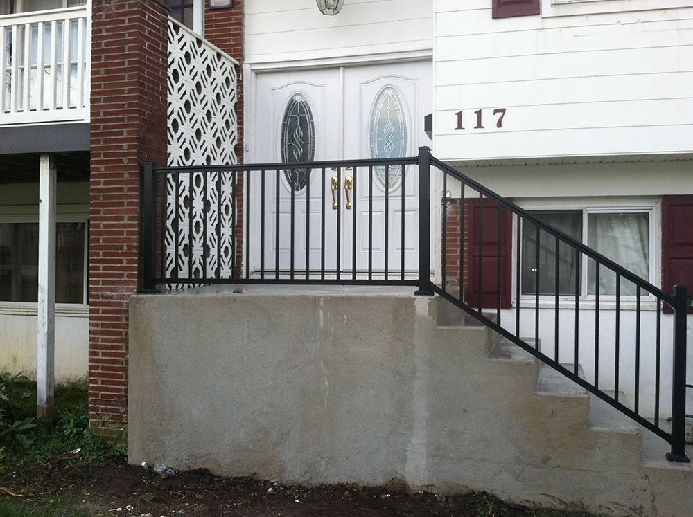 Black metal railing on a concrete front porch with steps leading to a white door. The house number is 117.