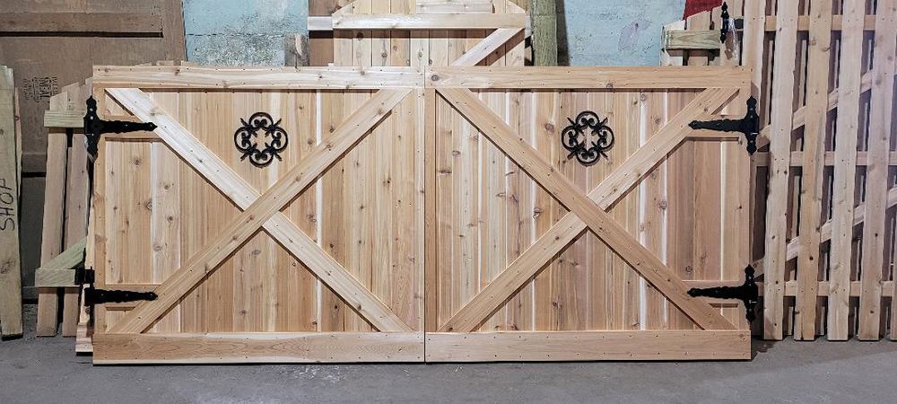 Wooden double gate with decorative ironwork, crossed supports, and black hinges.