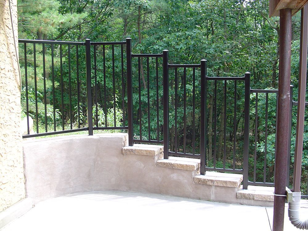 Black metal railing on a stone-faced, multi-level patio with forest background.
