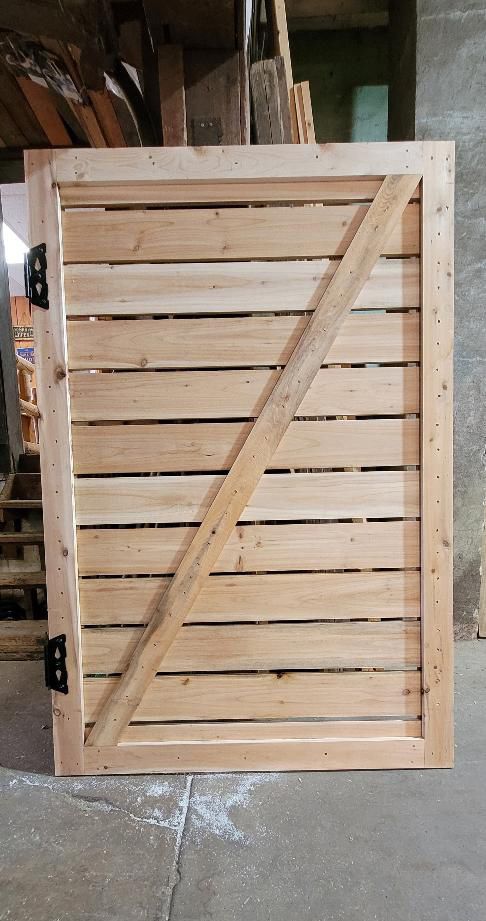 Wooden gate made of horizontal slats, diagonal support, and black hinges.
