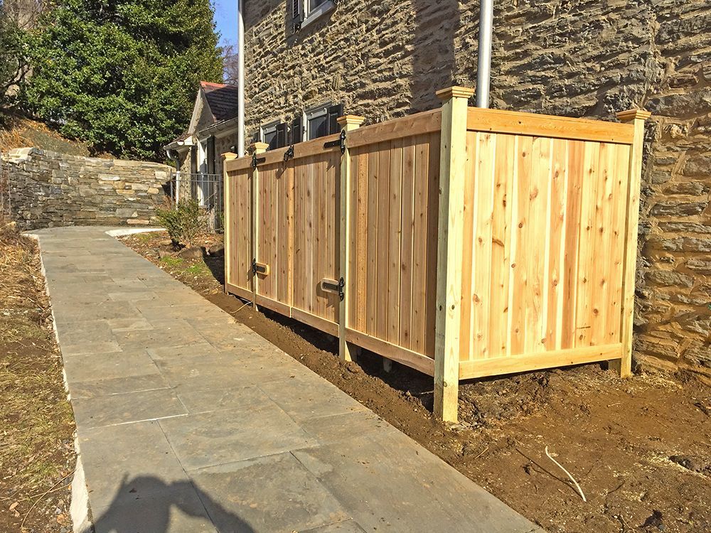 Wooden fence beside a stone building and paved walkway.
