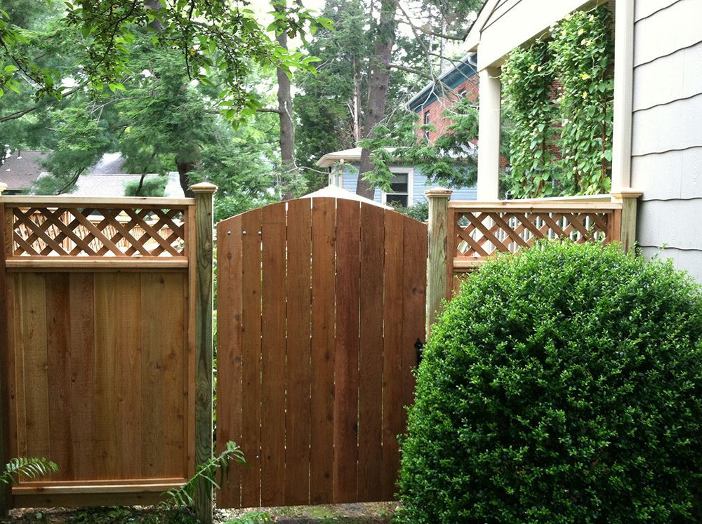 Wooden gate in a cedar fence with lattice details, leading into a yard with greenery.