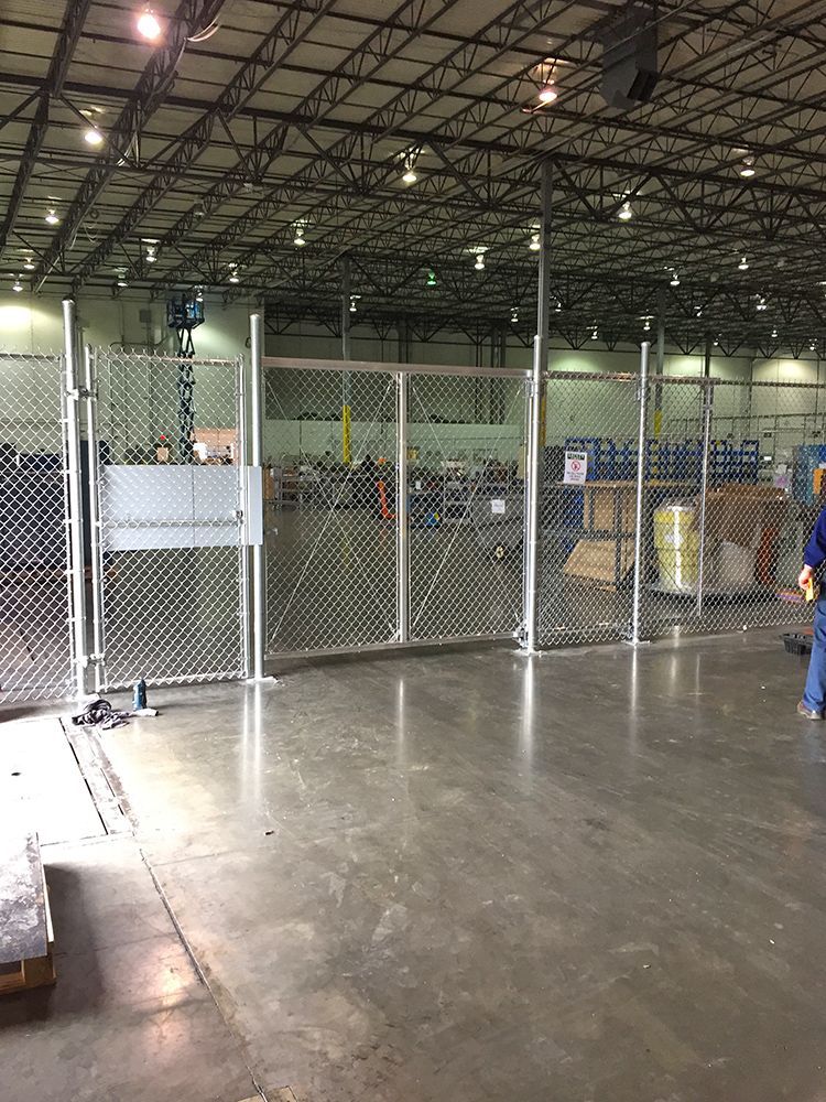 Chain-link fence security enclosure inside a large warehouse. Open gates and a person is visible near the enclosure.