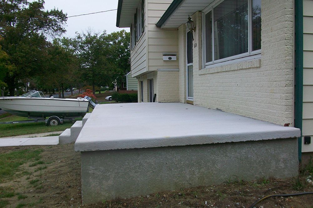 Concrete porch and steps leading to a two-story house with a boat parked nearby.